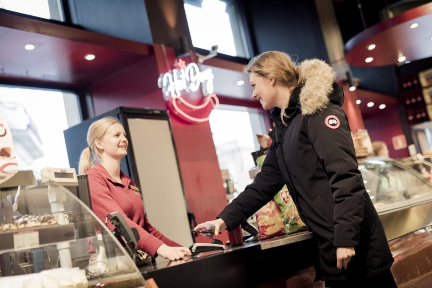 Dame betaler med mobil på kortterminal i kiosk. foto